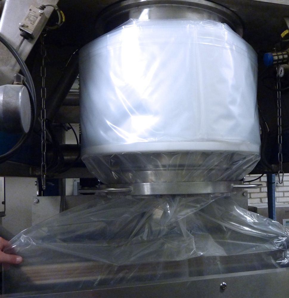 HECHT filling head with continuous liner system, illustrating a white, inflated polyethylene liner secured beneath a stainless steel drum, part of a powder handling and packaging operation designed for containment and cleanliness.