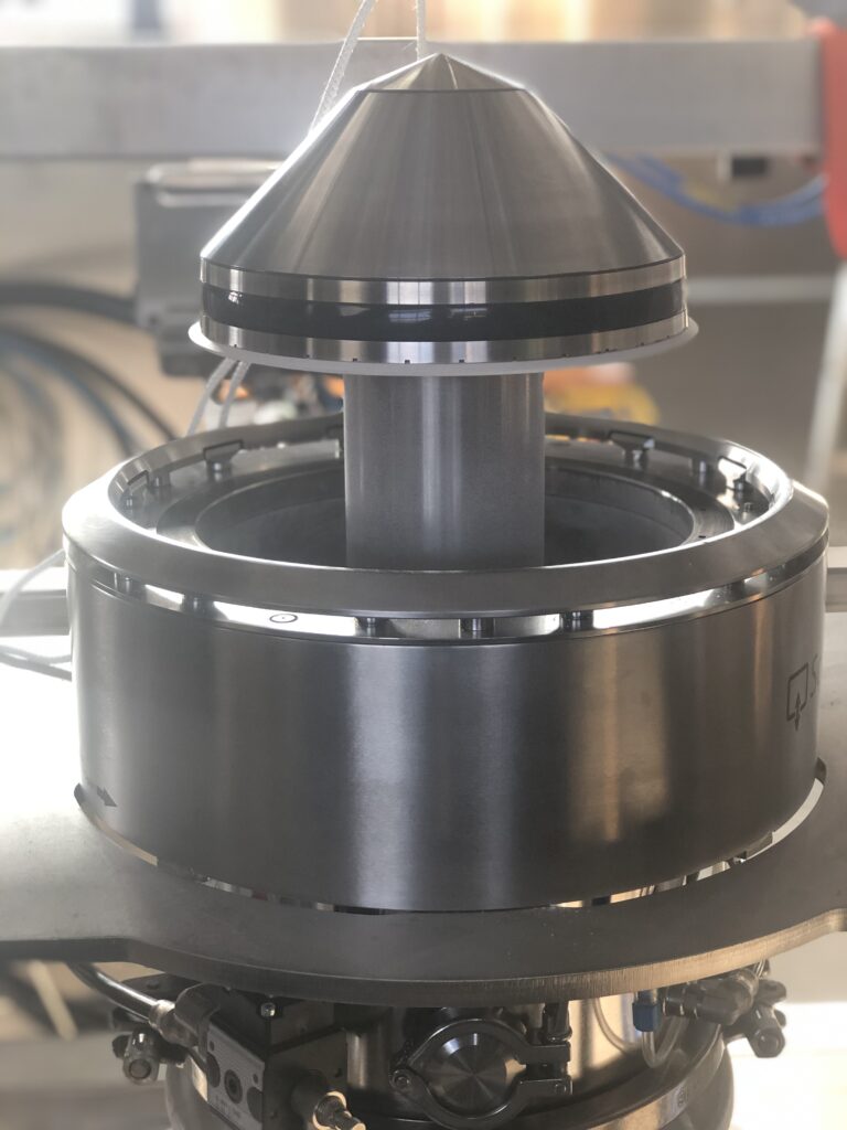 The HECHT SoliValve® system, shown with its conical plug element partially inserted into the docking station, demonstrates the precision of this powder handling technology. The metallic sheen of the stainless steel emphasizes the clean and advanced design suitable for controlled and contained material transfer.