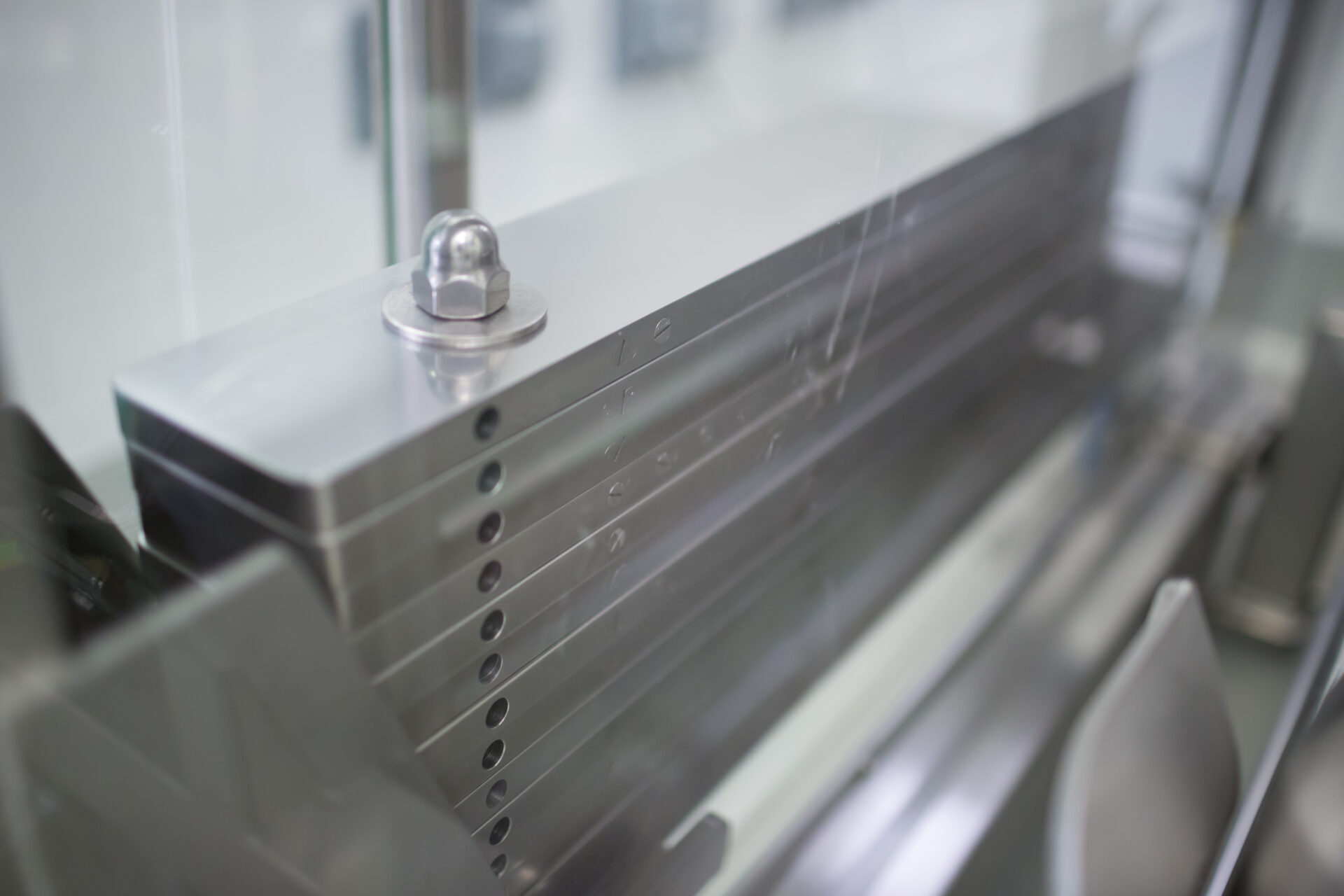 Close-up of a stainless steel component from a HECHT BigBag Discharge Station, showcasing a sleek metal surface with precision-drilled holes and fasteners, reflecting the meticulous engineering and robust construction of industrial-grade machinery.