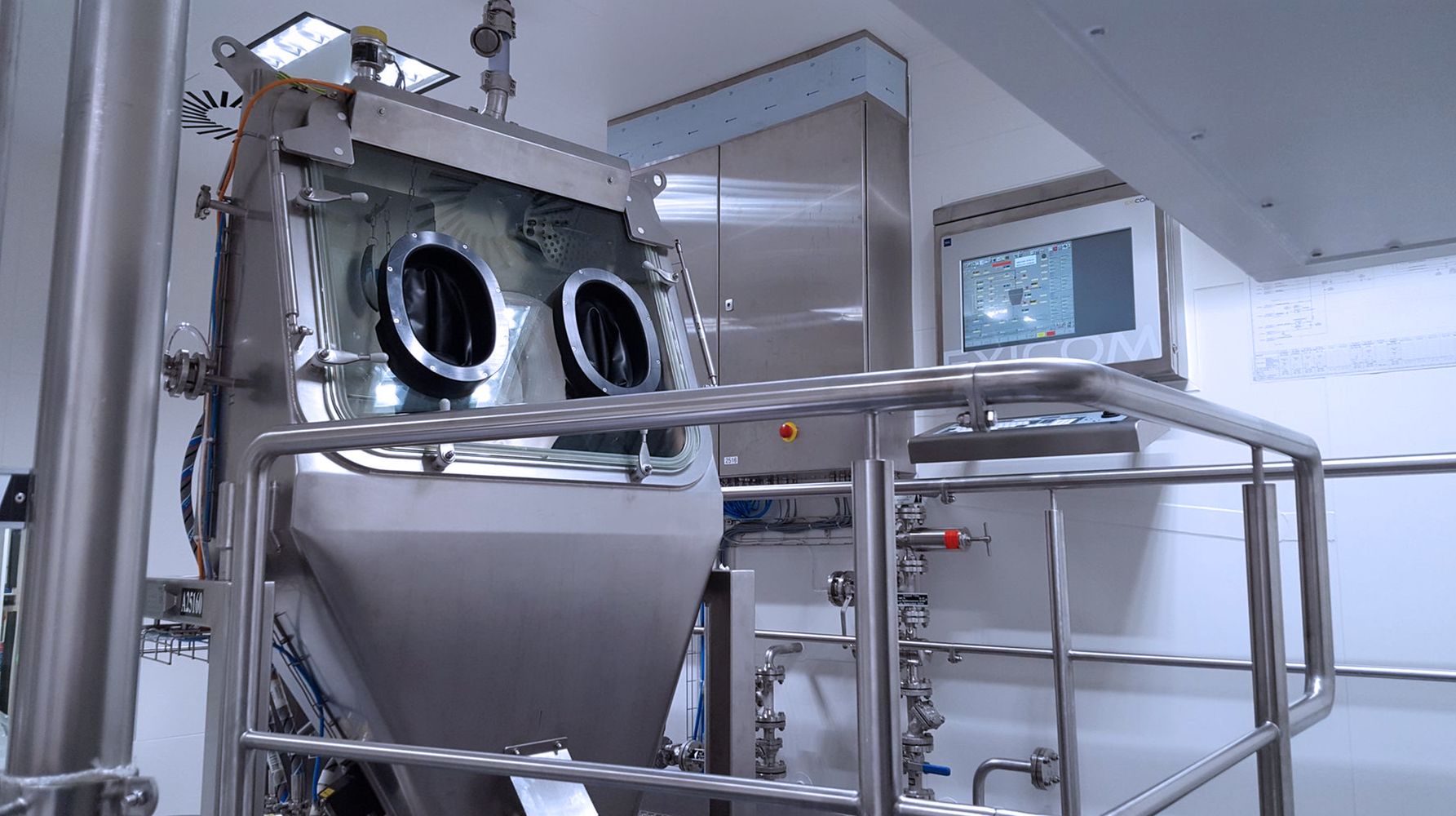 A HECHT Technologie Containment Drum Discharger installed in a cleanroom environment, featuring glove ports for secure handling, a control panel display, and a network of pipes and valves, all within a stainless steel frame.
