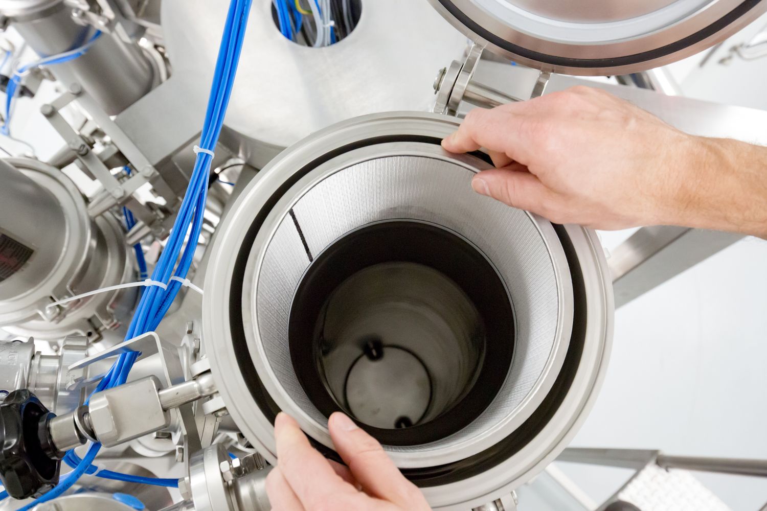 A person's hands carefully placing or inspecting a cylindrical filter element within a HECHT filtration system, highlighting the precision and maintenance aspect of industrial equipment. The focus on the filter's texture and the surrounding stainless steel components emphasizes the cleanliness and quality control in process environments.